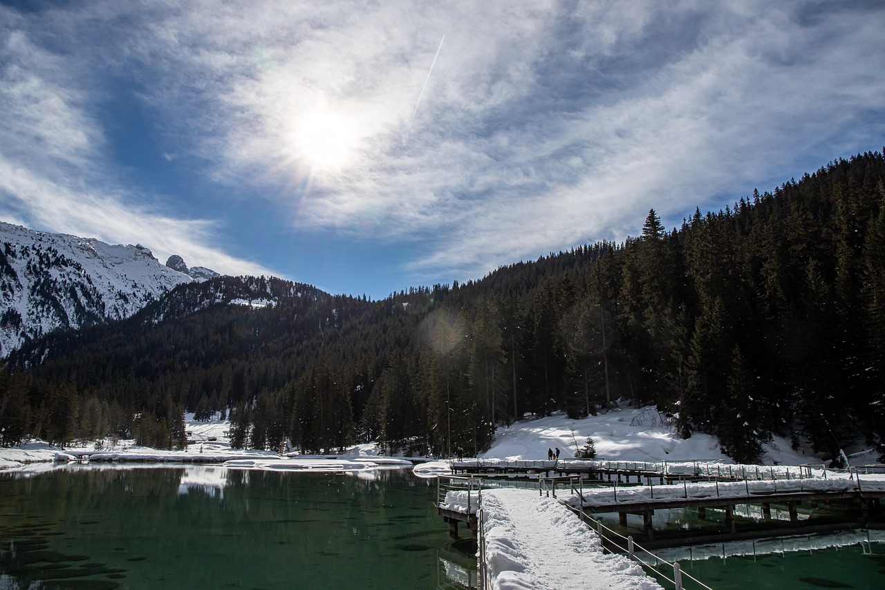 Lago di Carezza con il Latemar riflesso nelle acque cristalline, circondato da pini e montagne.